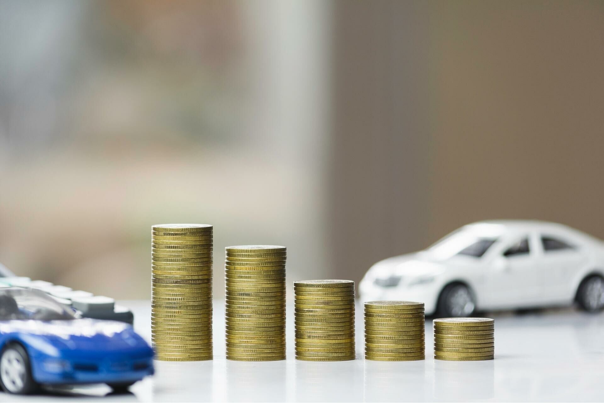 Miniatura de carros ao lado de pilhas de moedas