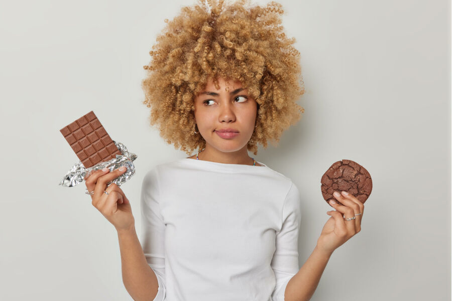 Imagem mulher-confusa-pensativa-escolhe-entre-chocolate-e-biscoito-tem-guloso-vestido-com-sueter-casual-mantem-dieta-sente-tentacao-de-comer-deliciosos-alimentos-prejudiciais-isolados-sobre-fundo-branco