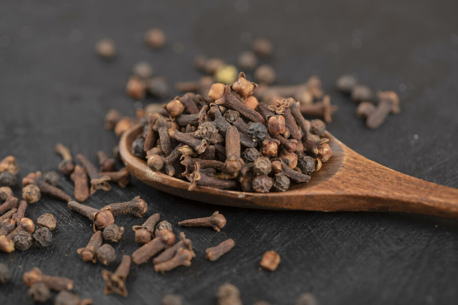 Imagem pilha-de-cravo-da-india-natural-seco-com-colher-de-pau-na-superficie-preta